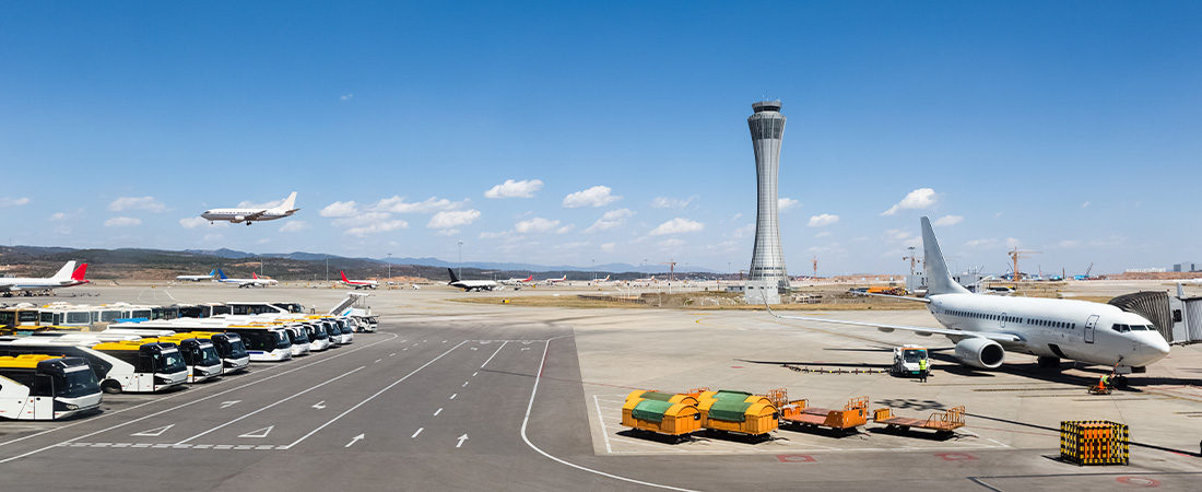 Vista panorámica de la pista de un aeropuerto concurrido, con múltiples aviones estacionados en las puertas de embarque y una torre de control al fondo.