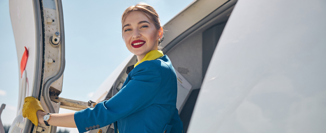 Azafata de vuelo sonriendo desde la puerta de entrada de un avión