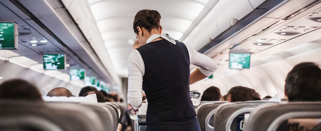 Tripulante de cabina atendiendo pasajeros en el pasillo del avión.
